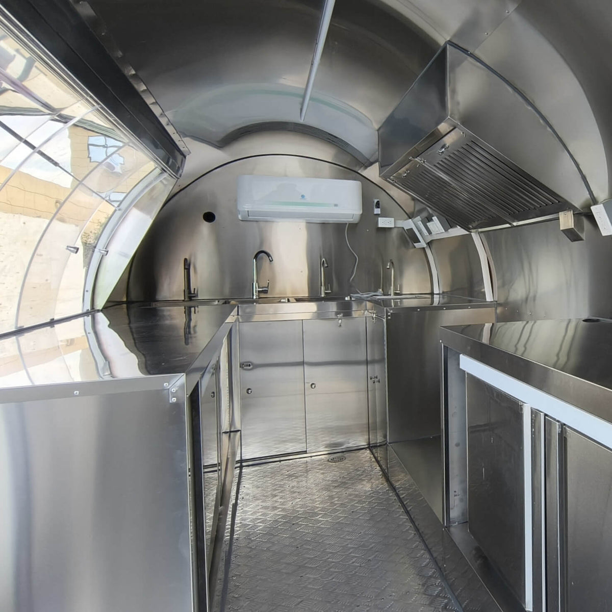 Bakery trailer stainless steel interior with curved sliding window, sink, plumbing, and preparation workspace