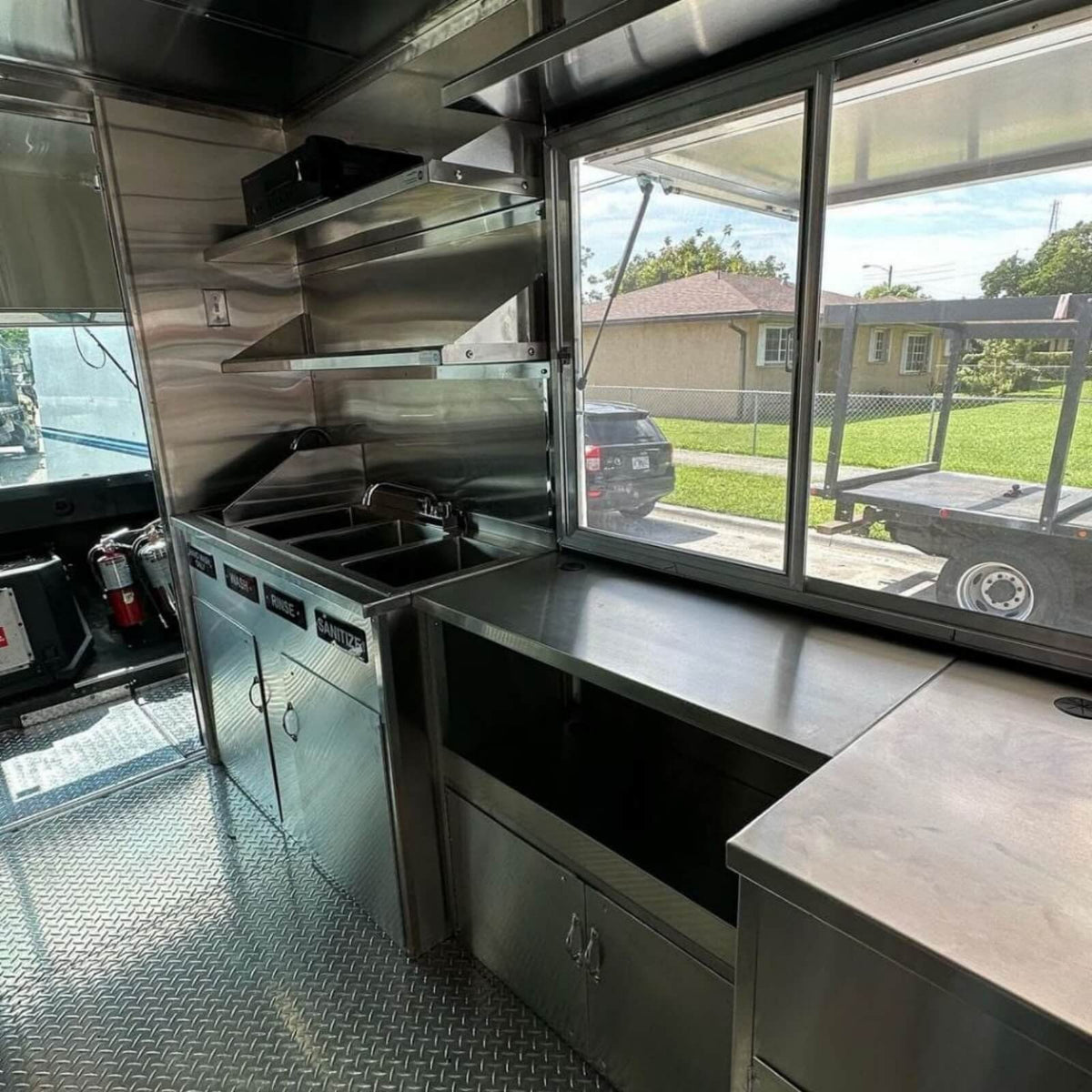 BBQ food truck interior with 3-compartment sink, stainless steel worktable and sliding serving window – NSF-compliant mobile kitchen