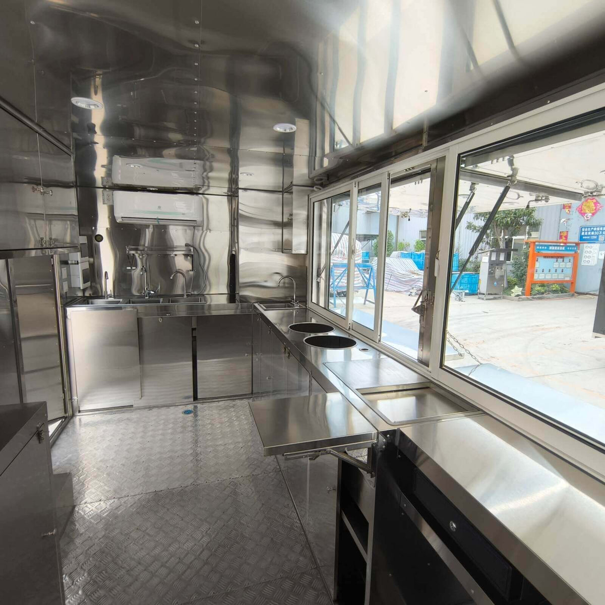 Stainless steel interior of a custom beverage trailer with open service windows, sliding panels, and commercial workspace