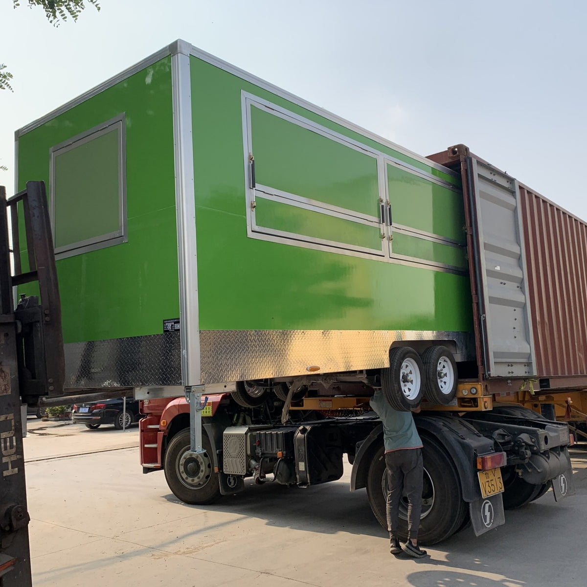 Green concession trailer loaded on flatbed truck for export shipping – factory direct food trailer delivery worldwide