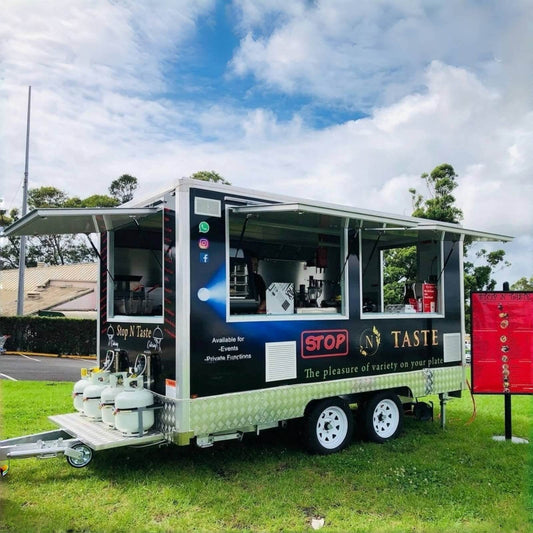 Custom food concession trailer with dual open service windows, front-mounted propane tanks, full graphic wrap, and a heavy-duty dual axle chassis.