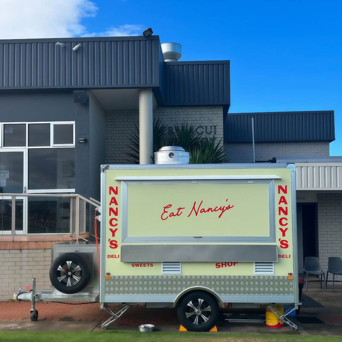 Custom small concession trailer with single axle square box design, cream yellow exterior wrap, large service window, stainless steel shelf, and commercial food trailer chassis.