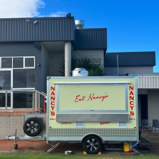 Custom small concession trailer with single axle square box design, cream yellow exterior wrap, large service window, stainless steel shelf, and commercial food trailer chassis.